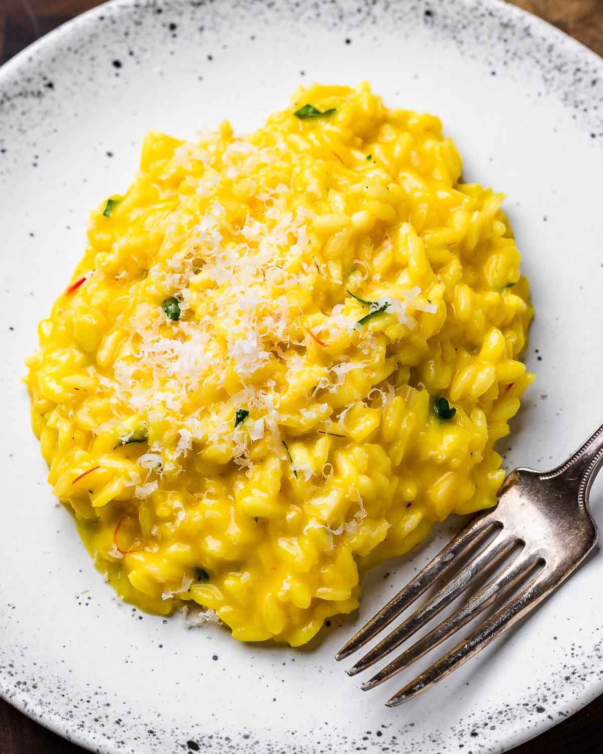 Overhead shot of white plate with Risotto alla Milanese topped with shaved Parmigiano Reggiano cheese.