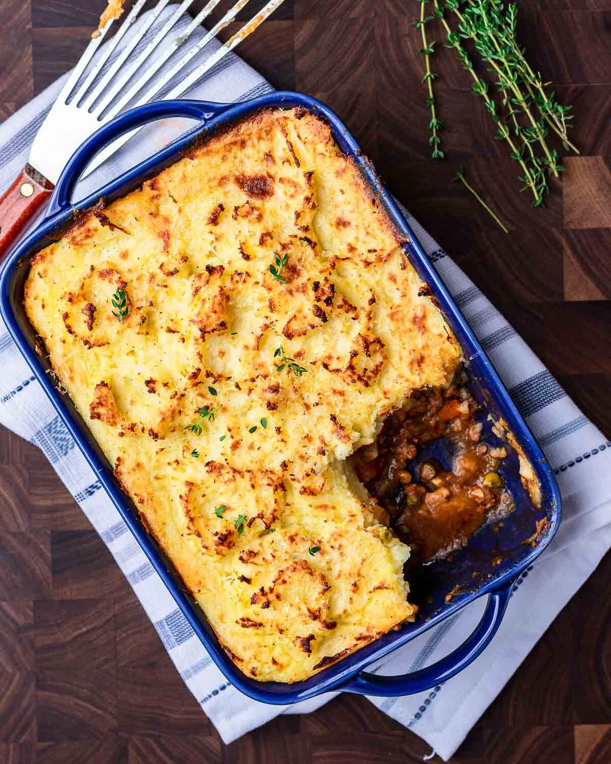 Ovehead shot of shepherd's pie in blue dish with one slice taken out of it.