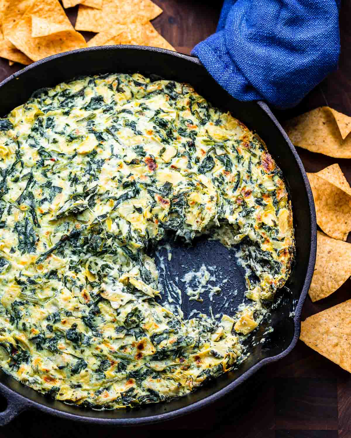 Overhead shot of cast iron pan with spinach artichoke dip and tortilla chips.