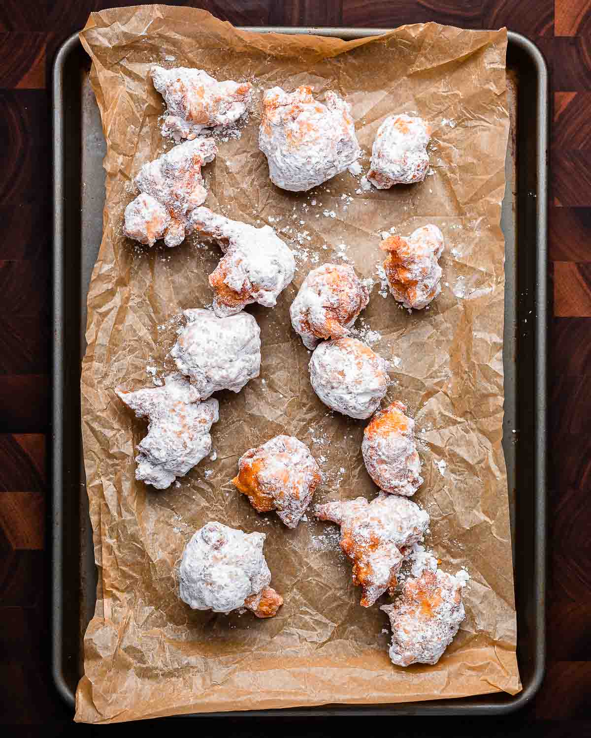 Overhead shot of fried zeppole on parchment paper lined baking sheet.