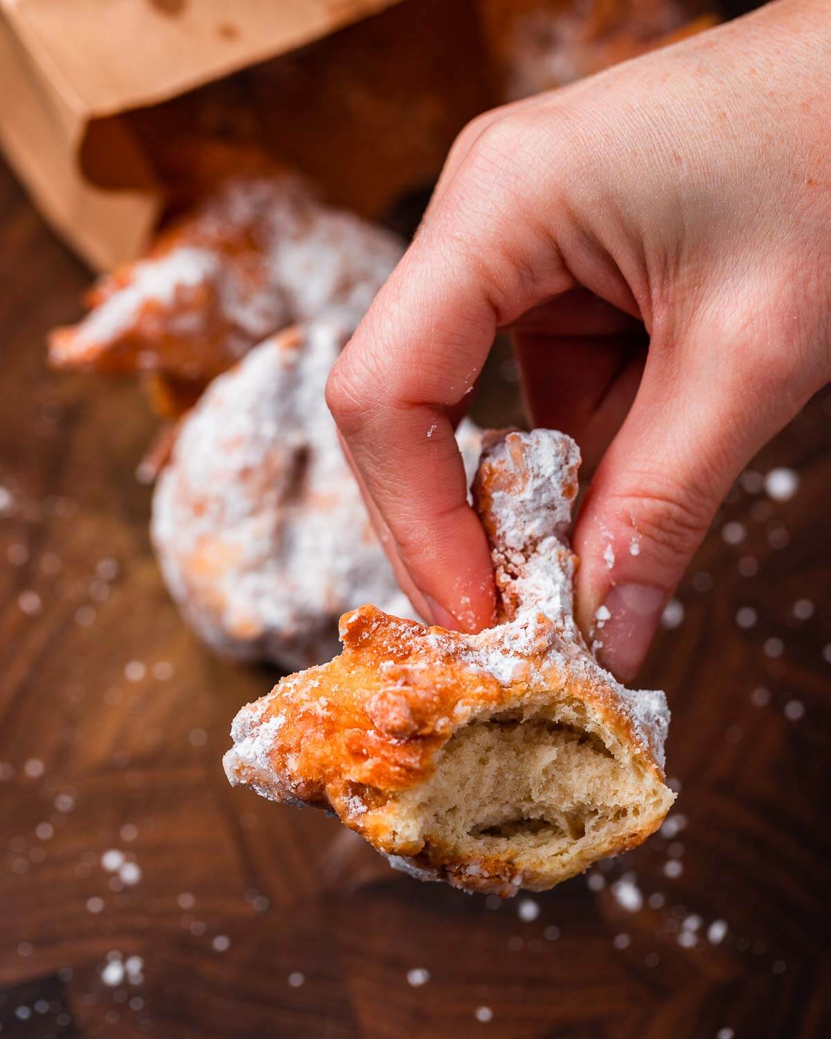 Hands holding zeppole with bite taken out of it.