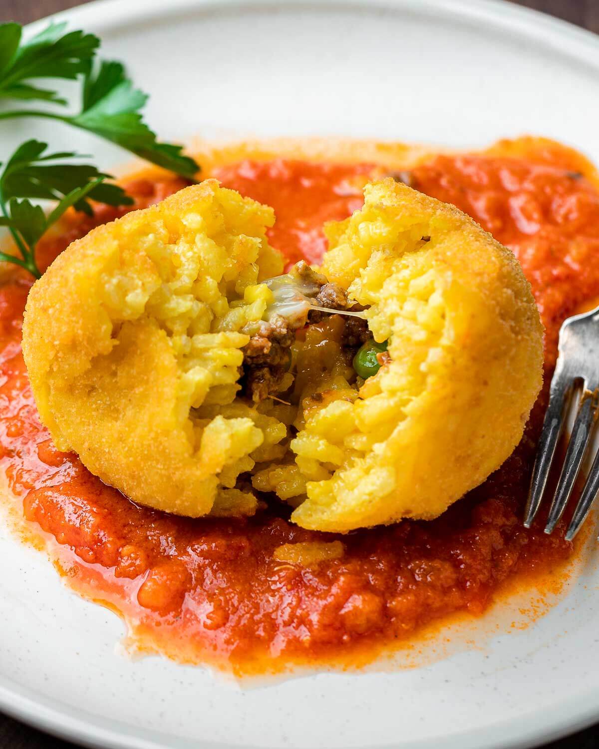 Closeup shot of arancini split open on top of sauce.