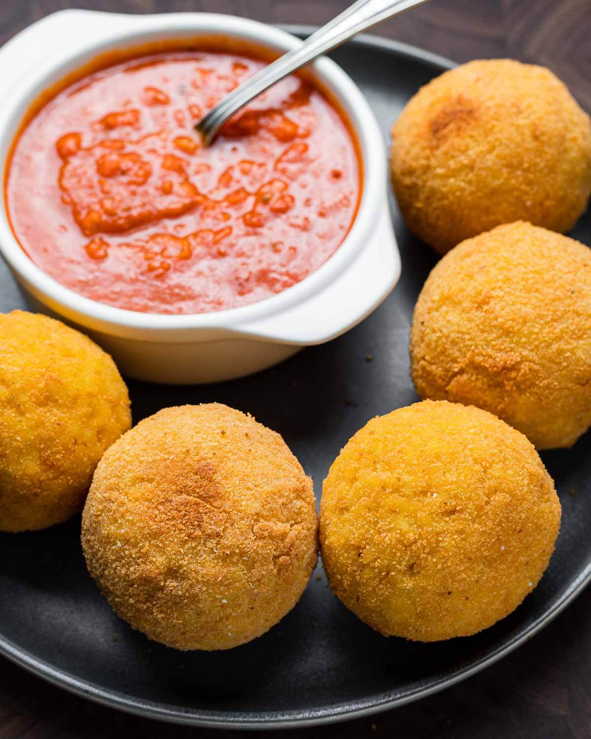 Grey plate with arancini and bowl of sauce.