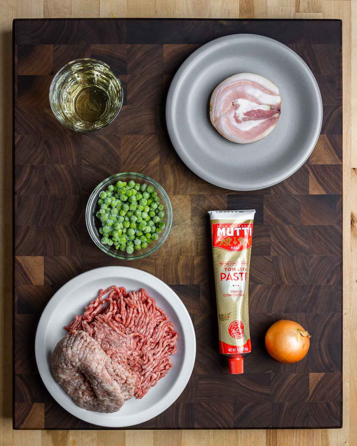 Ingredients shown: white wine, pancetta, peas, ground beef and ground pork, tomato paste, and a small onion.