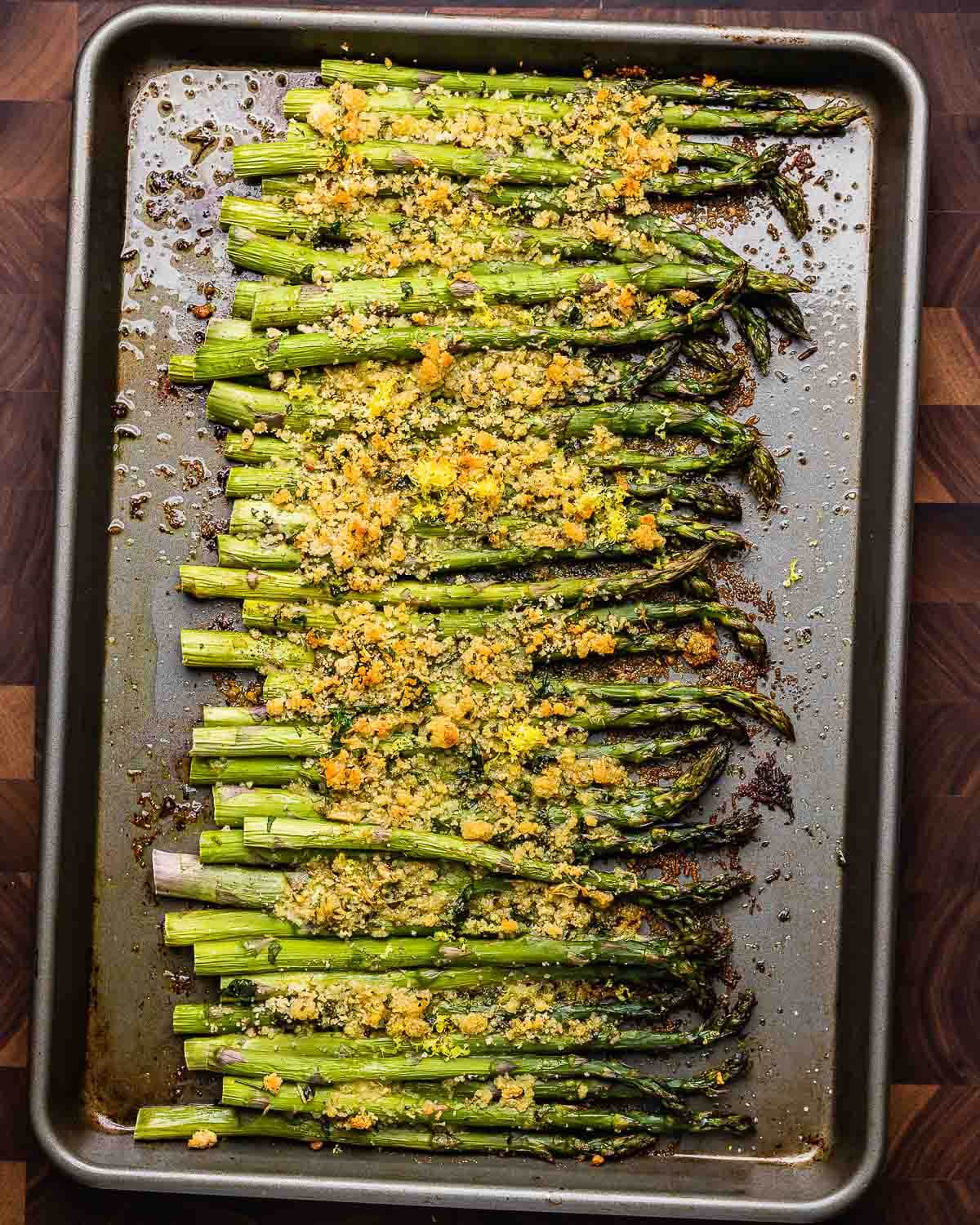 Overhead shot of baked asparagus with cheese and breadcrumbs on baking sheet.