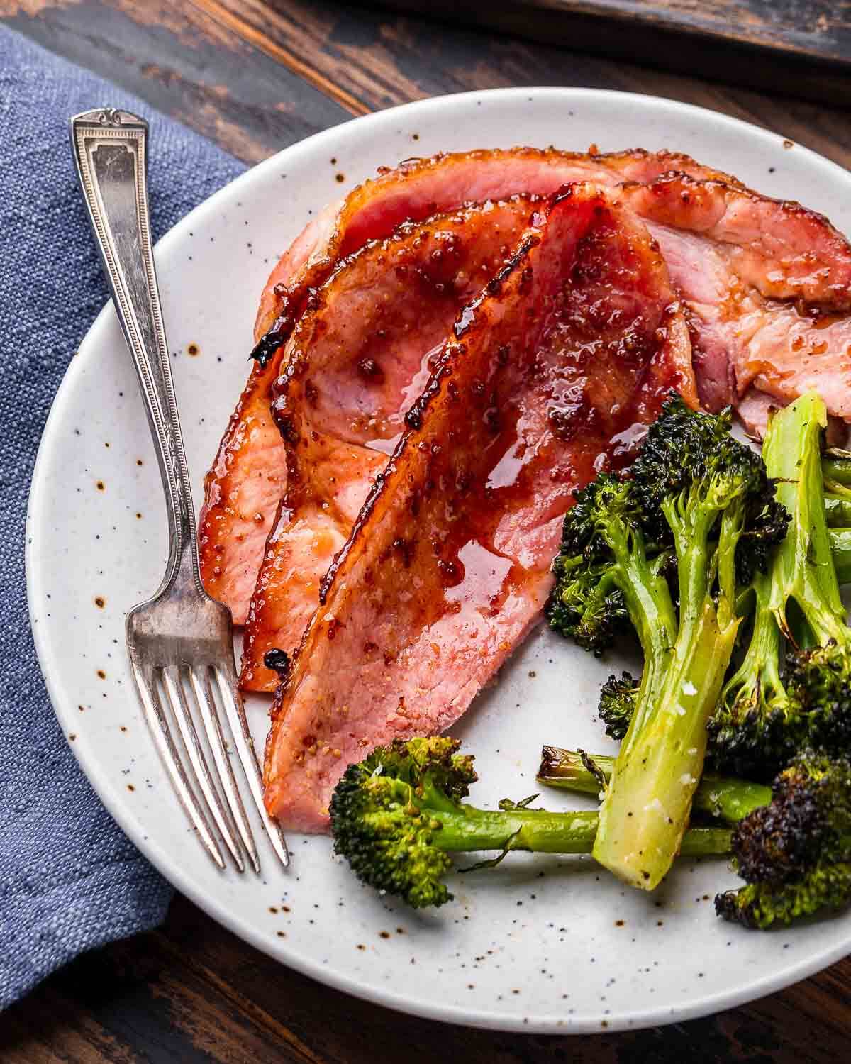 White plate with brown sugar glaze ham and broccoli.