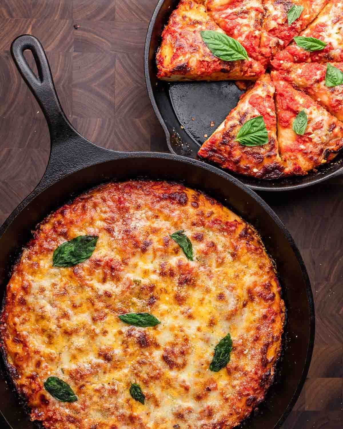 Overhead shot of 2 cast iron pan pizzas on walnut cutting board.