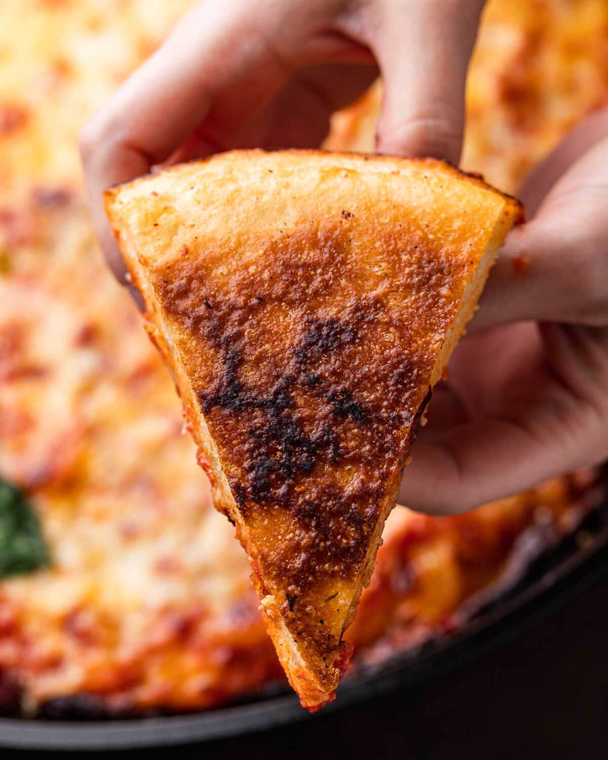 Hands holding slice of cast iron pizza turned over to show the golden bottom.