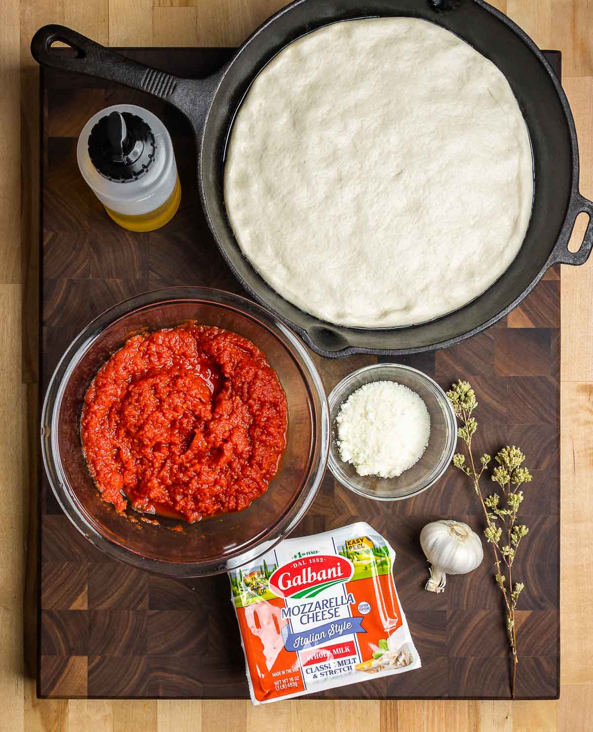 Ingredients shown: pizza dough in cast iron pan, olive oil. drained crushed tomatoes, Pecorino, mozzarella, garlic, and Sicilian oregano.