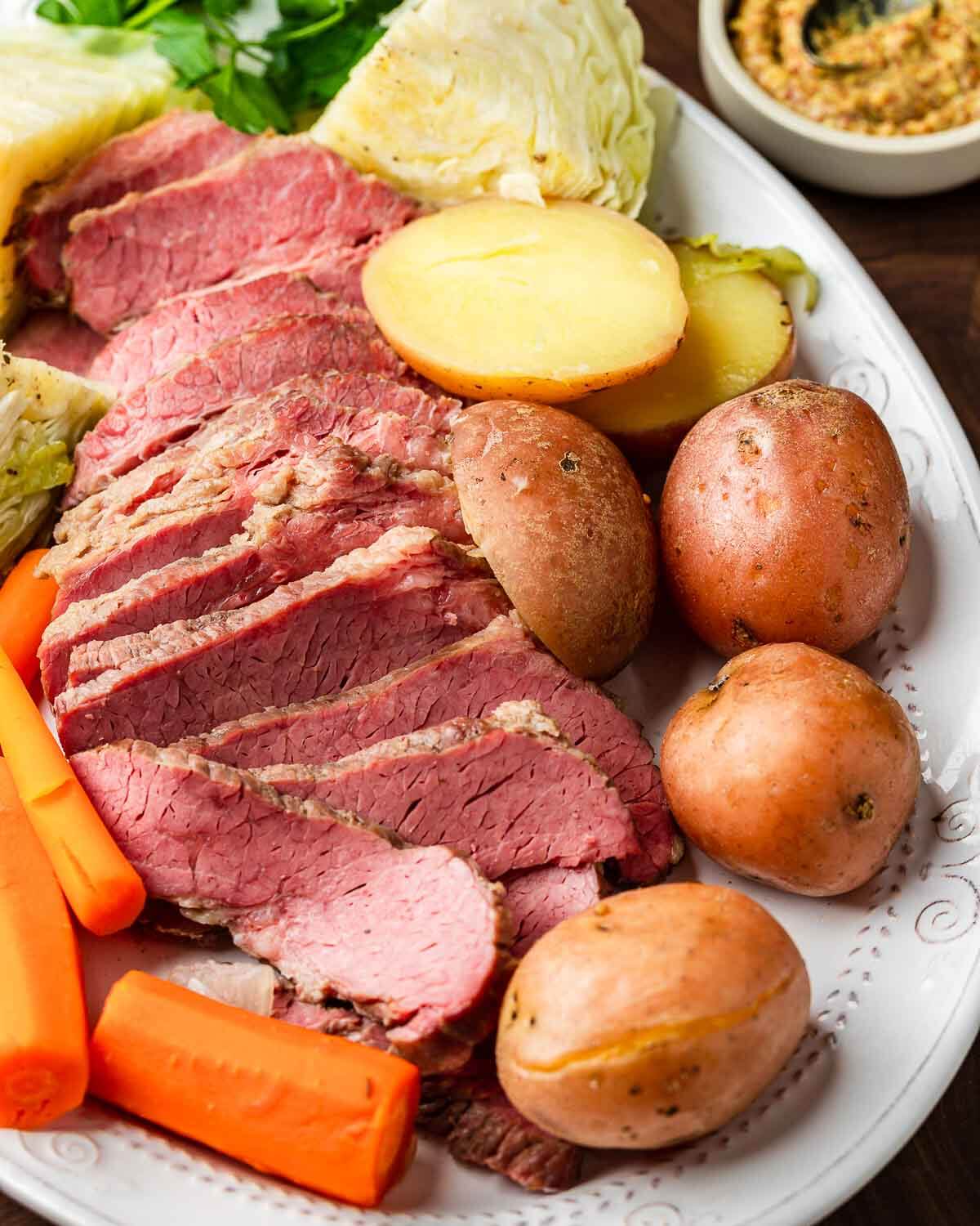 Platter with corned beef, cabbage, potatoes, and carrots with small bowl of mustard in the background.