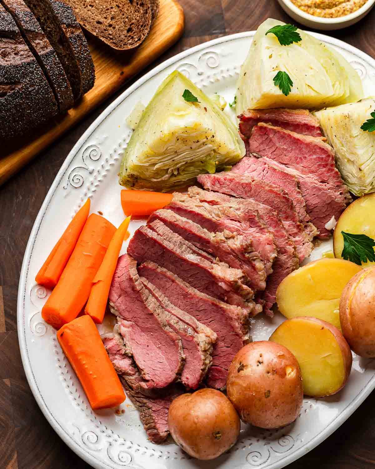 Overhead shot of platter with corned beef, cabbage, potatoes, and carrots with loaf of brown bread.