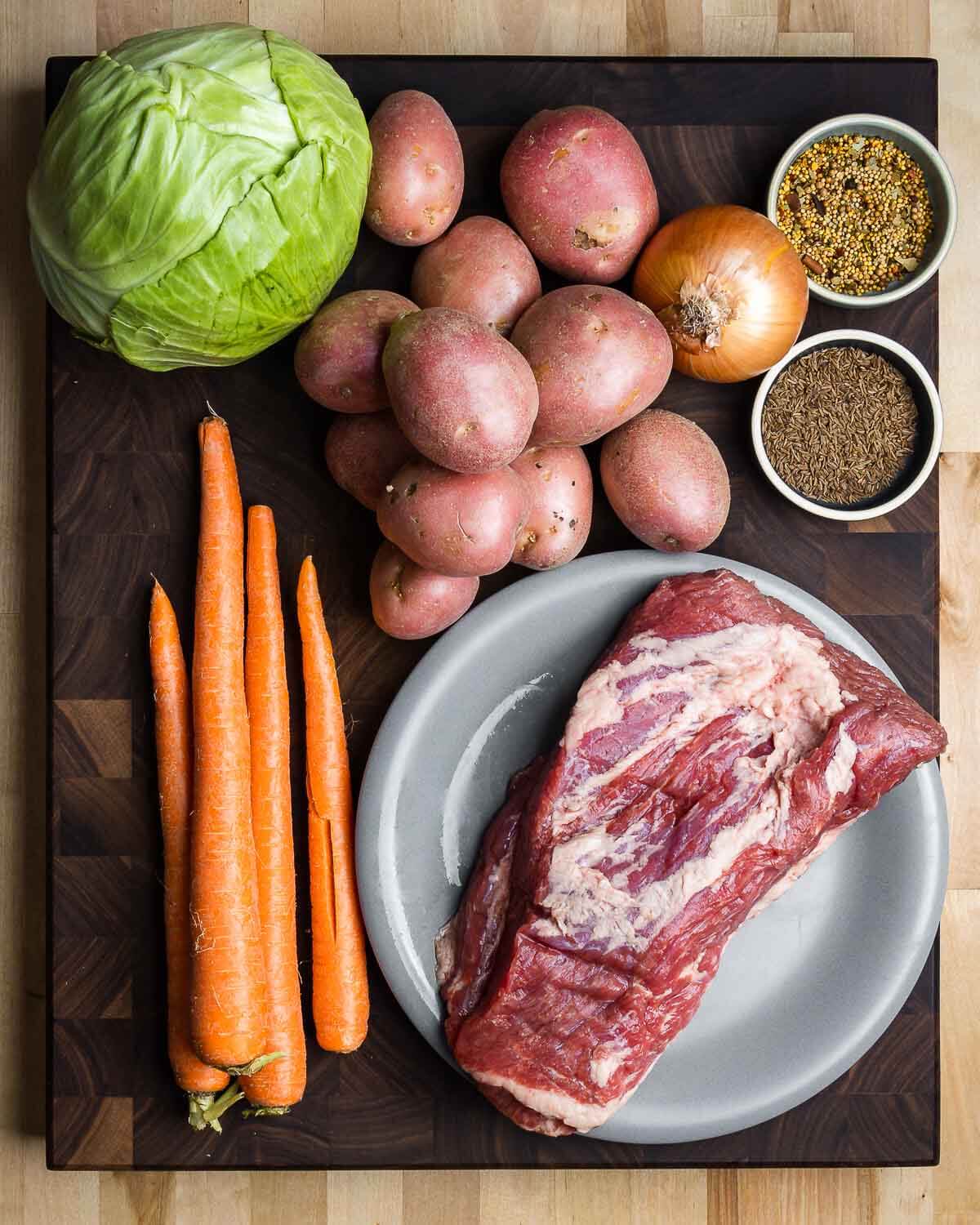 Ingredients shown: cabbage, potatoes, onion, pickling spice, caraway seeds, carrots, and corned beef.
