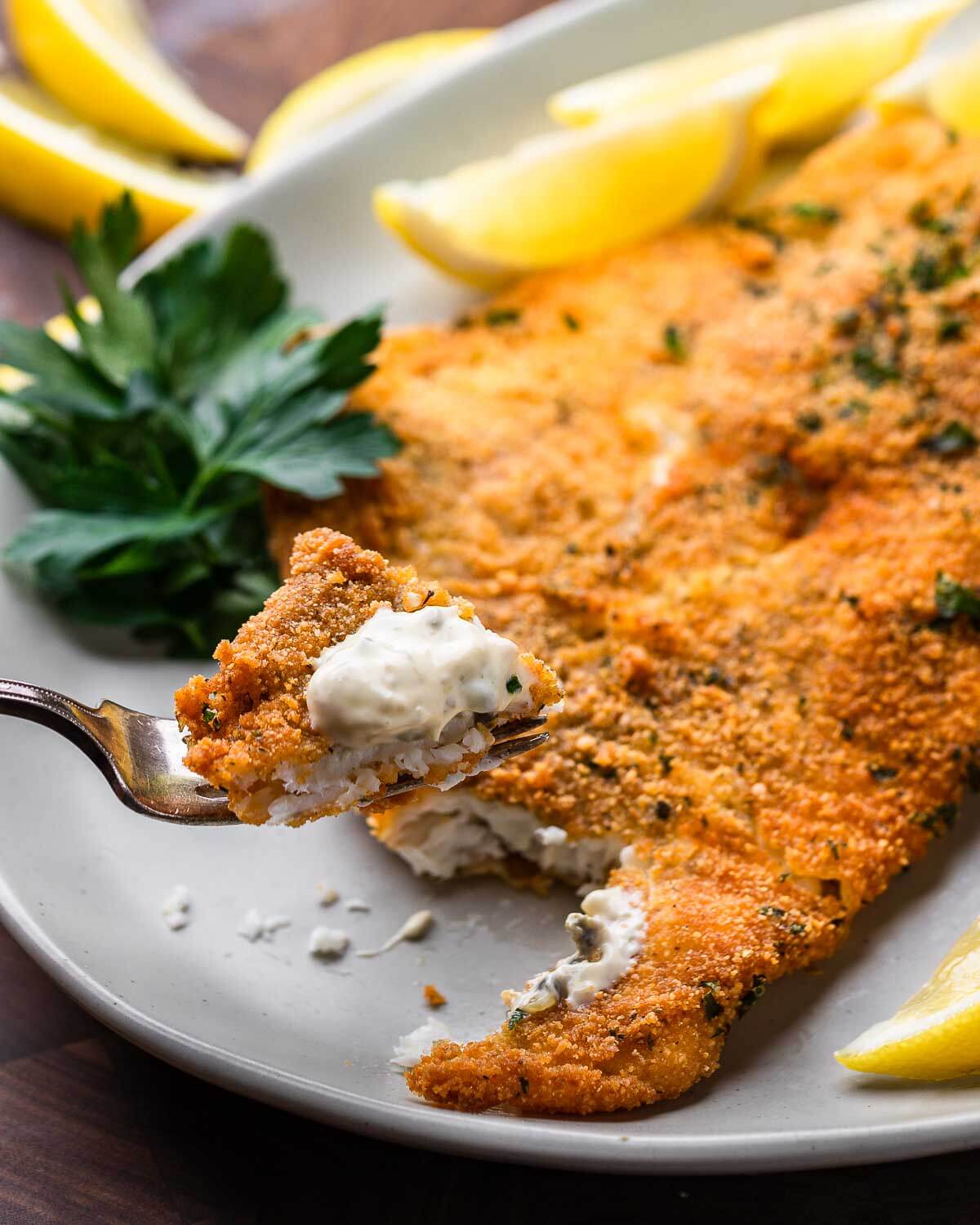 Fork holding piece of fried flounder with tartar sauce.