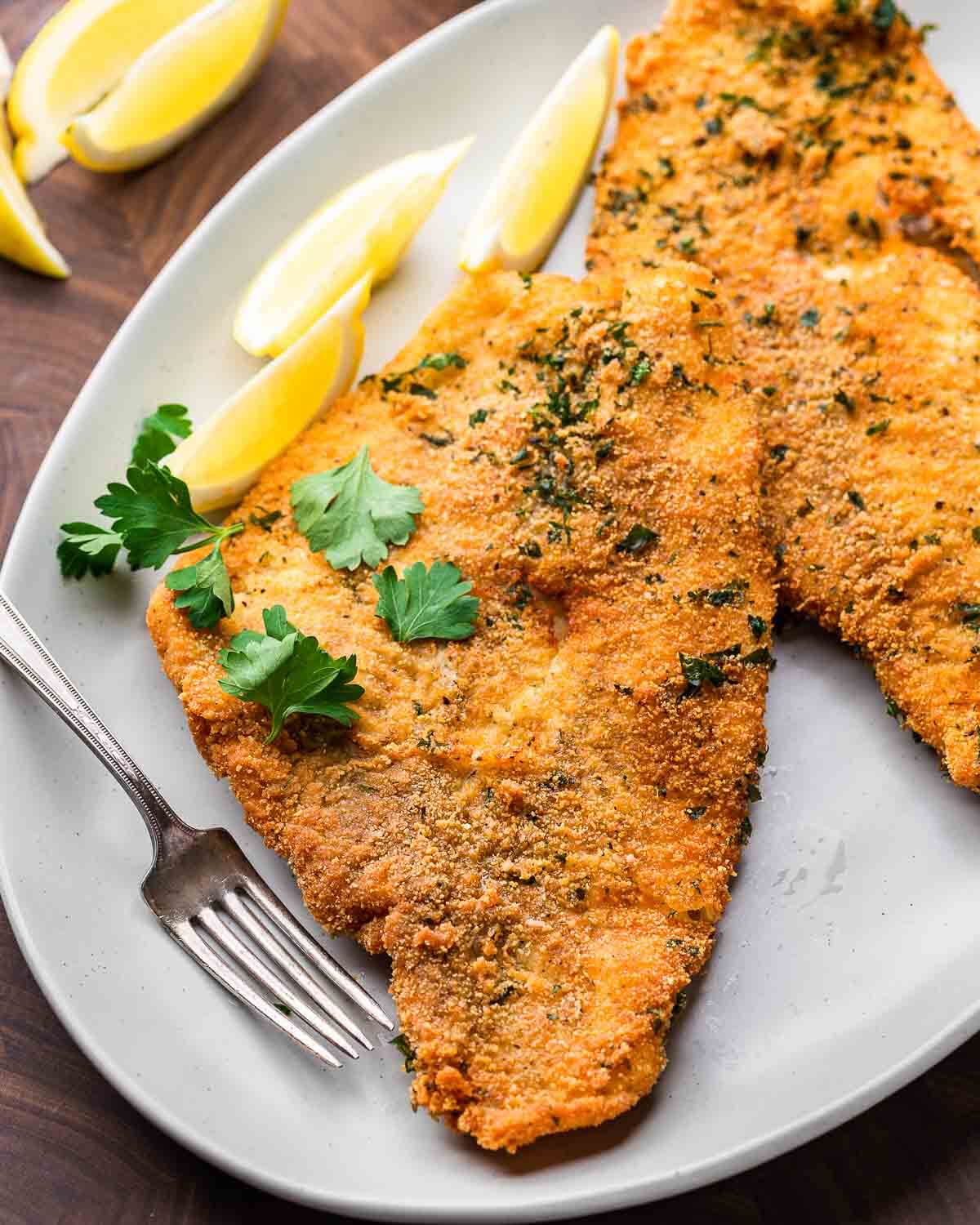 Platter of fried flounder with parsley garnish and lemon wedges.