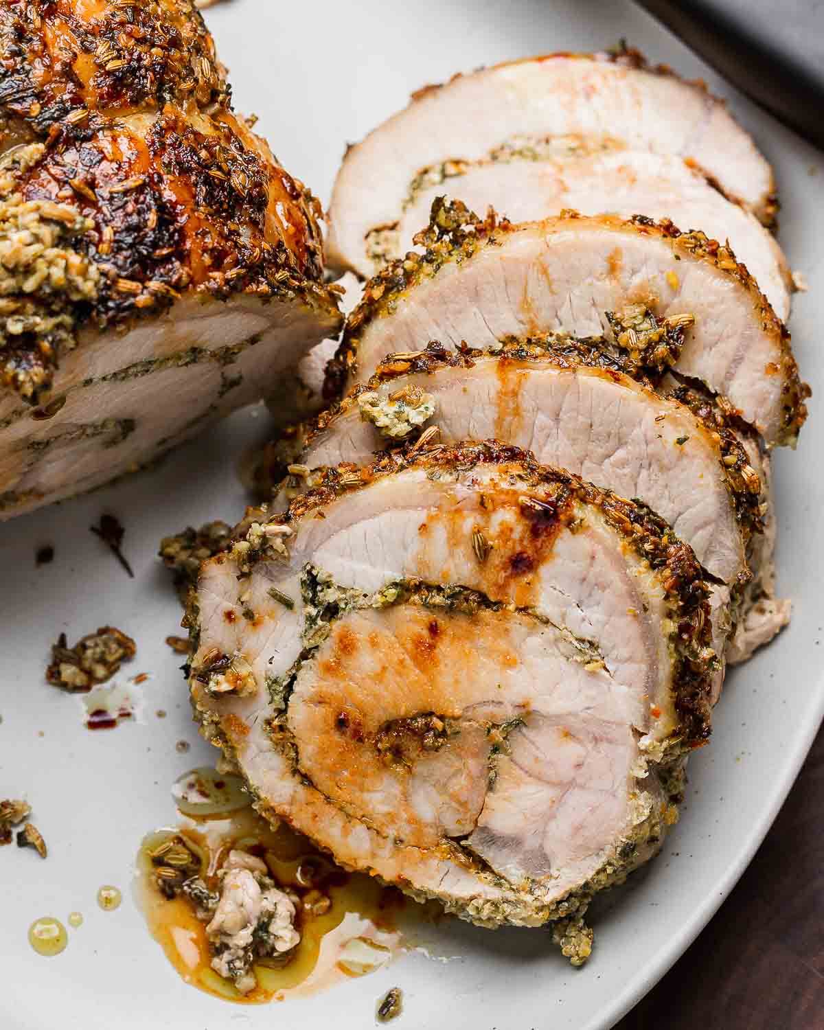 Four slices of Italian stuffed pork loin in white platter.