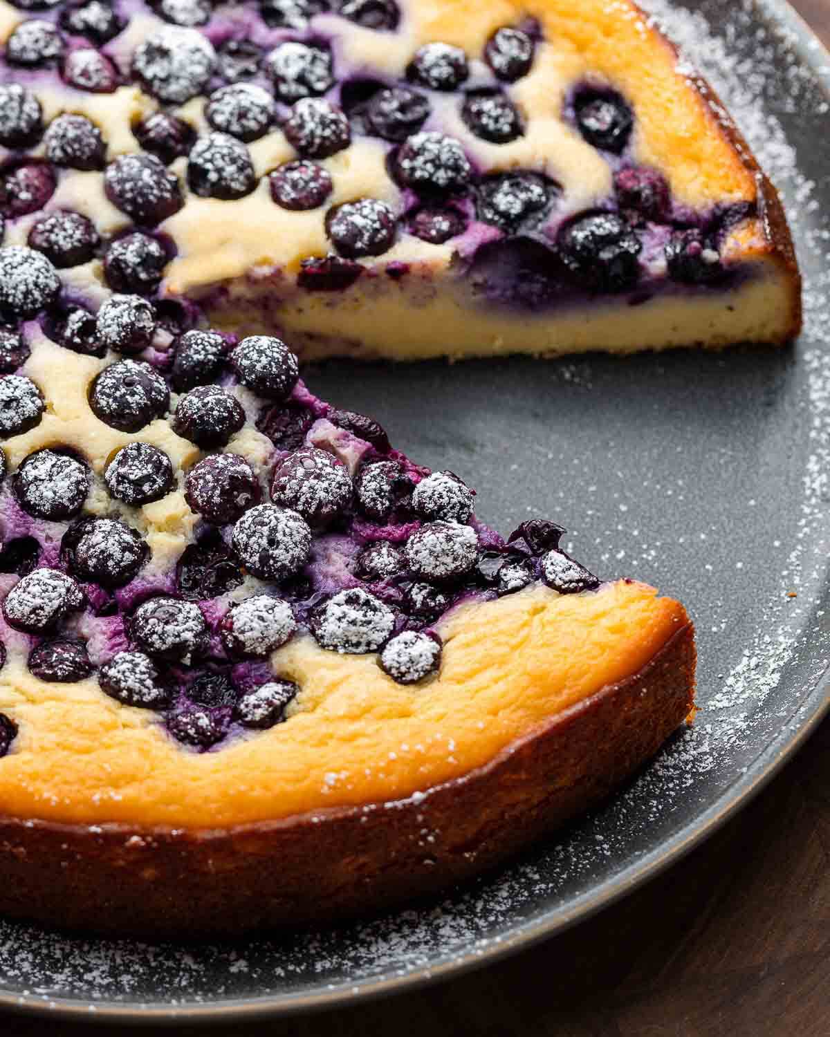 Blueberry ricotta cake on grey plate with 1 slice removed.