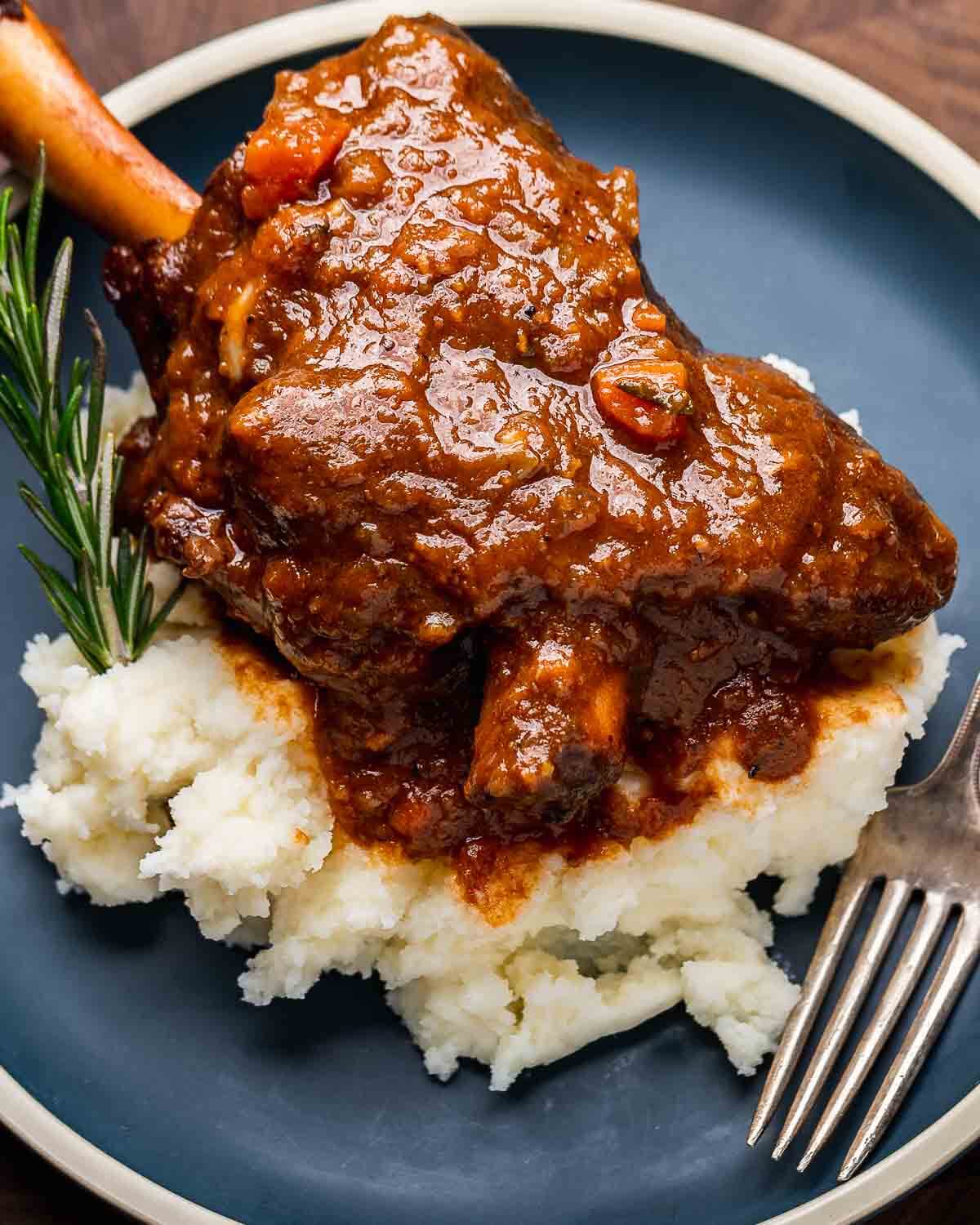 Closeup shot of red wine braised lamb shanks with mashed potatoes on blue plate.