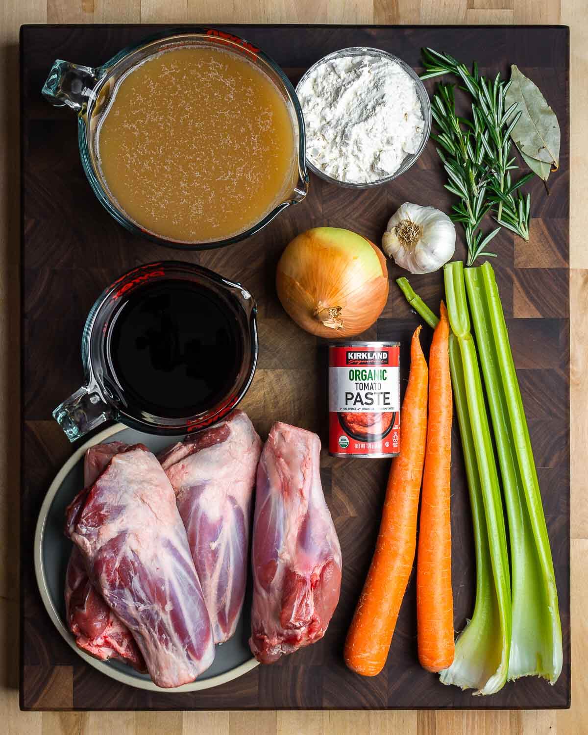 Ingredients shown: beef stock, flour, herbs, onion, garlic, red wine, tomato paste, carrots, celery, and lamb shanks.