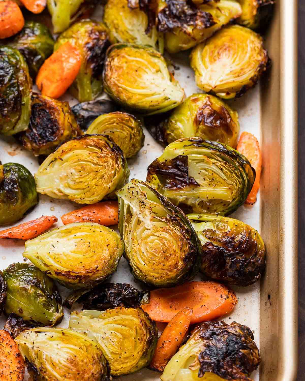 Closeup shot of roasted brussels sprouts and carrots in sheet pan.