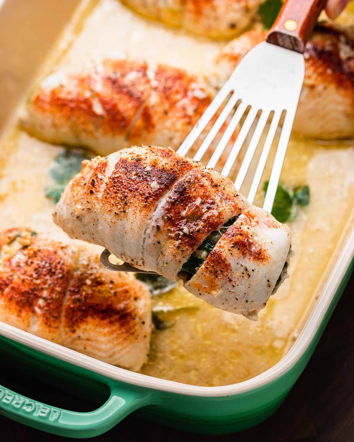 Spatula holding spinach stuffed flounder above baking dish.