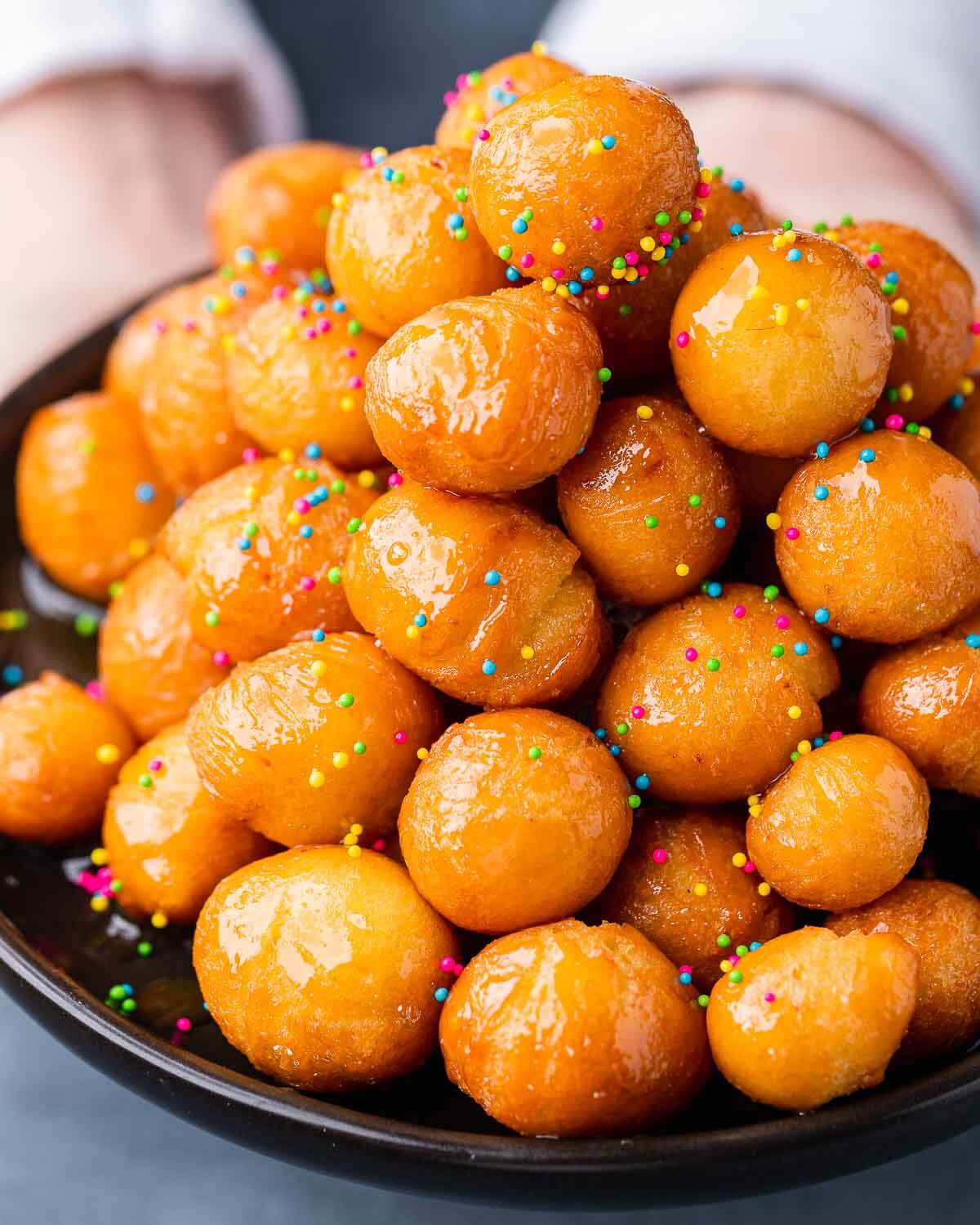 Hands holding black plate with a mound of struffoli.