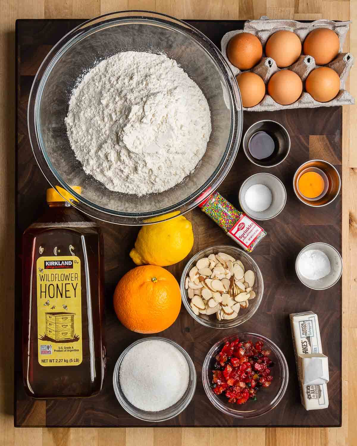 Ingredients shown: flour, eggs, vanilla, Gran Marnier, salt, baking powder, nonpareils, honey, orange, lemon, almonds, candied fruit, sugar, and butter.