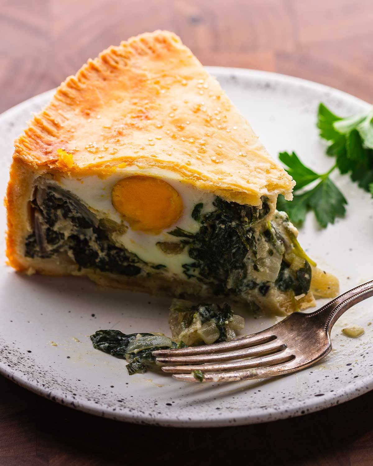 Slice of torta pasqualina in white plate with fork.