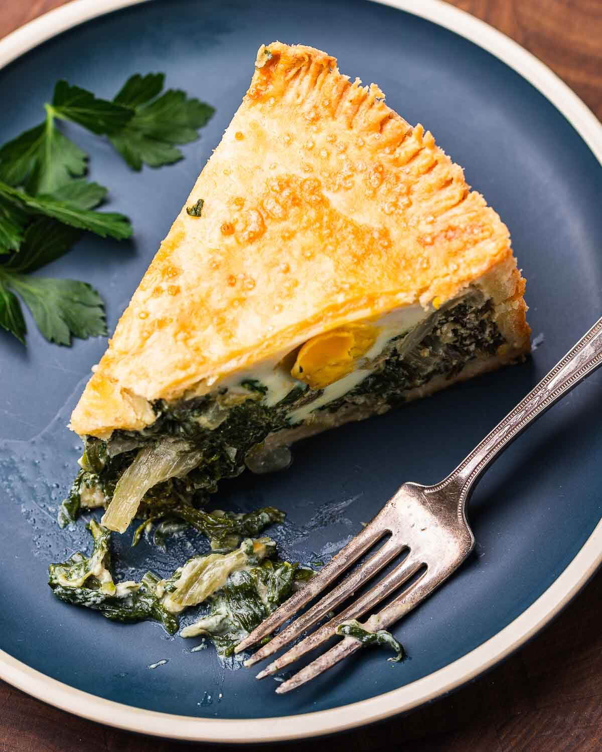 Slice of torta pasqualina in blue plate with fork.