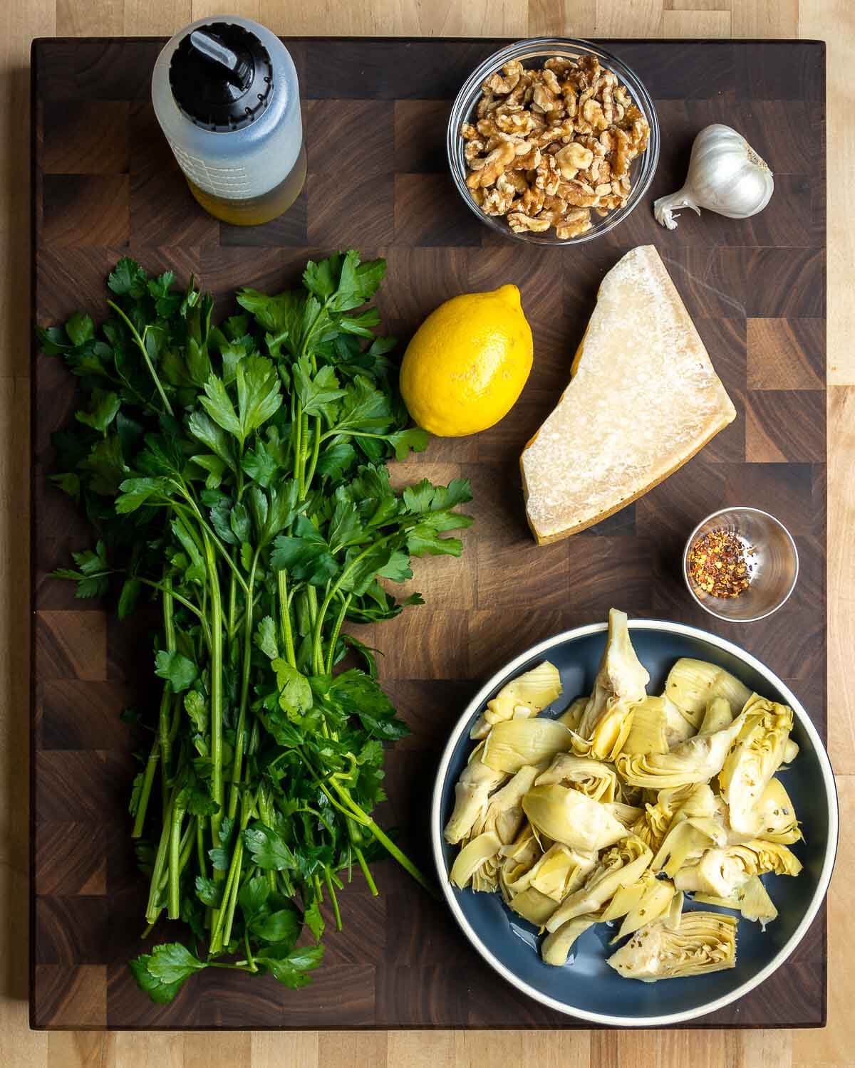 Ingredients shown: extra virgin olive oil, walnuts, garlic, parsley, lemons, Parmigiano Reggiano, hot red pepper flakes, and artichoke hearts.