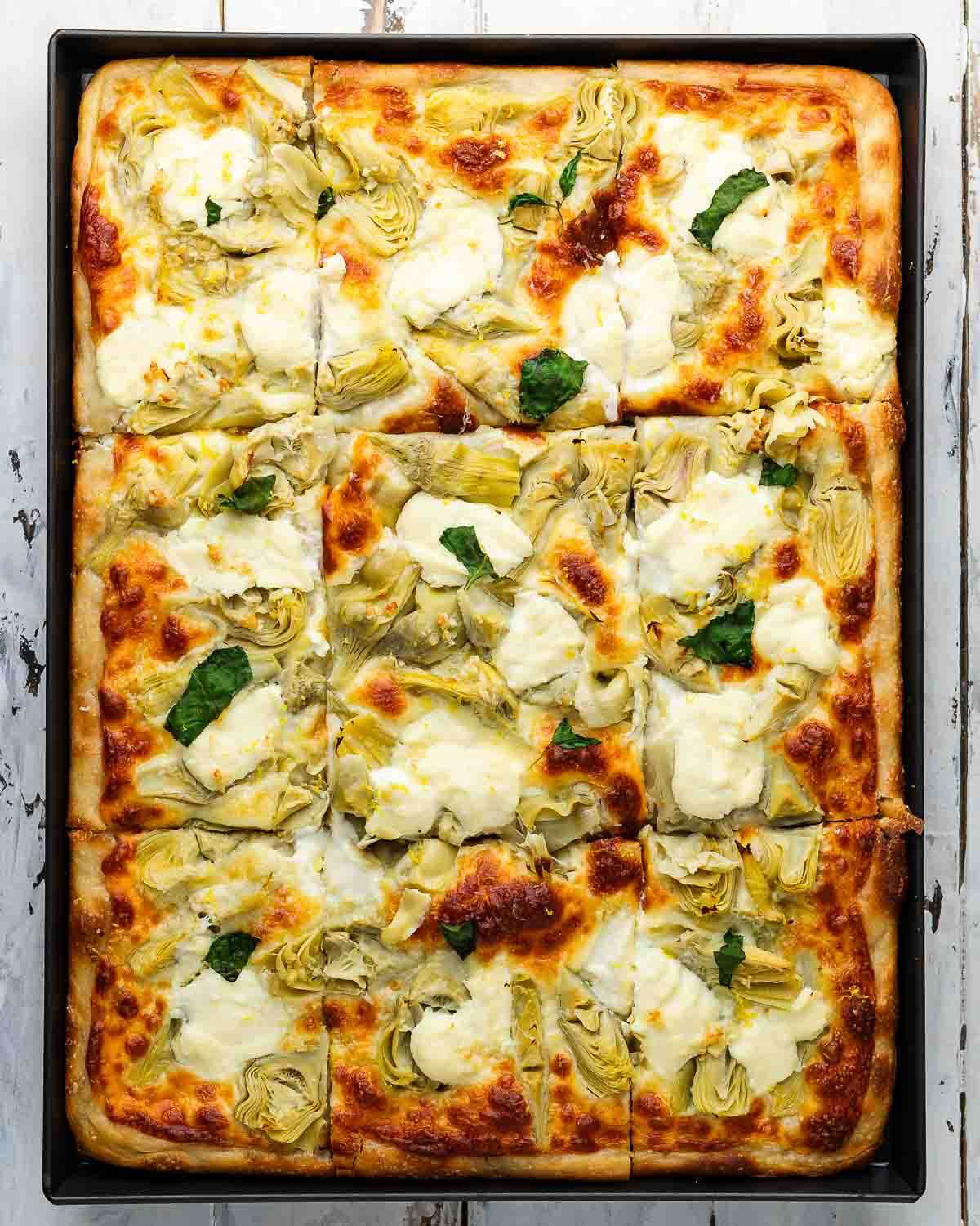 Overhead shot of artichoke sheet pan pizza on white board.