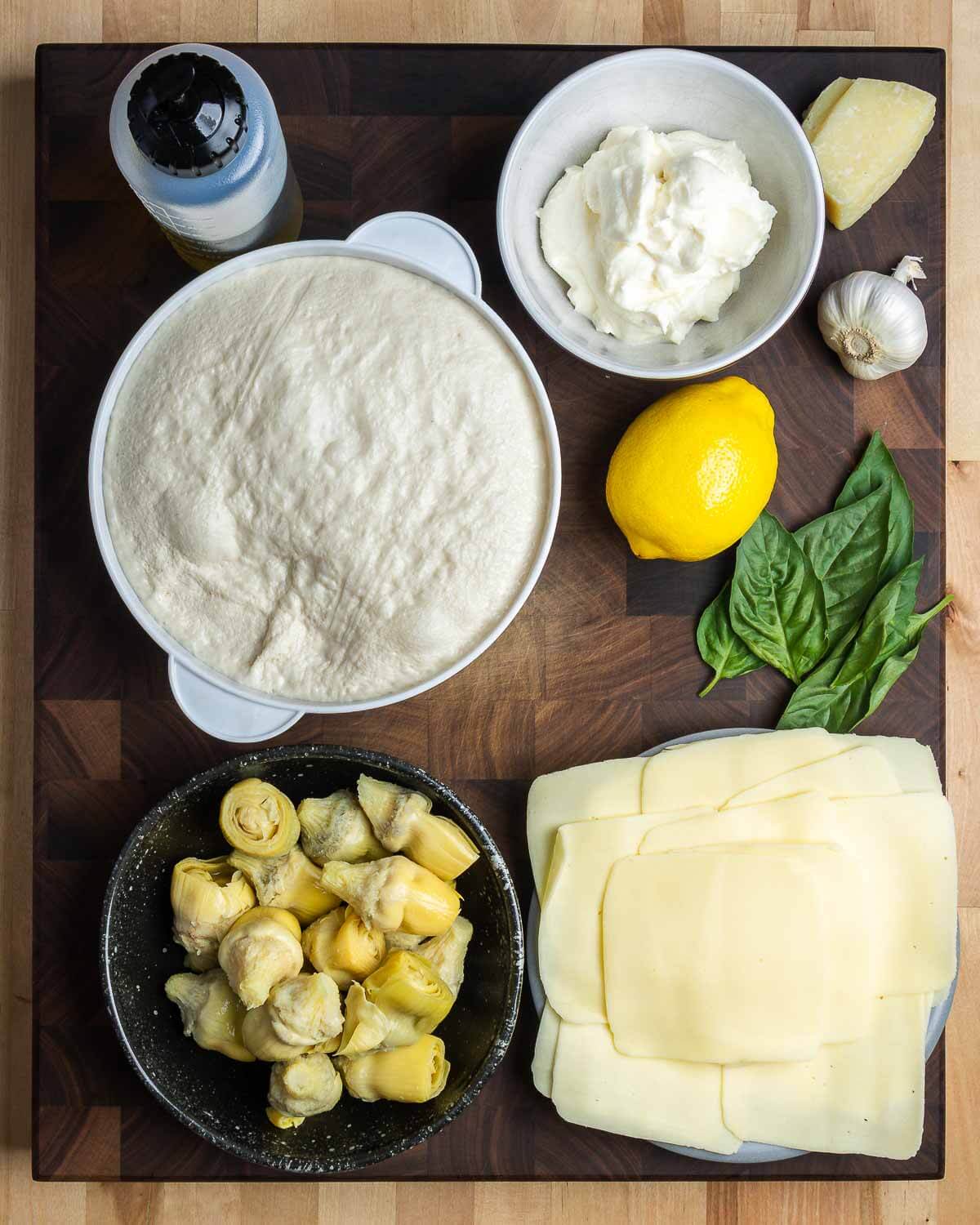 Ingredients shown: olive oil, pizza dough, ricotta, lemon, Pecorino, garlic, basil, artichoke hearts, and sliced mozzarella.