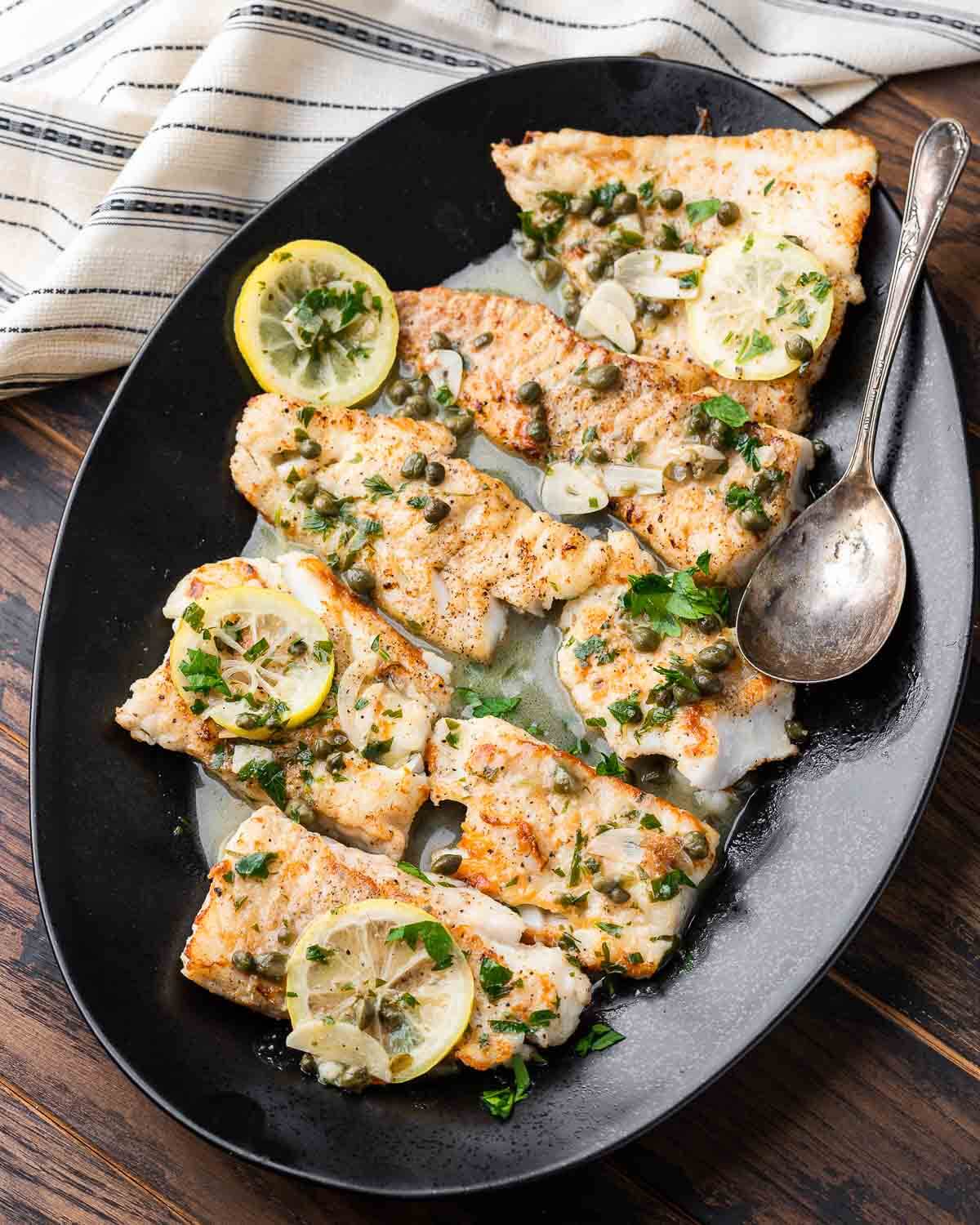 Overhead shot black platter with cod piccata.