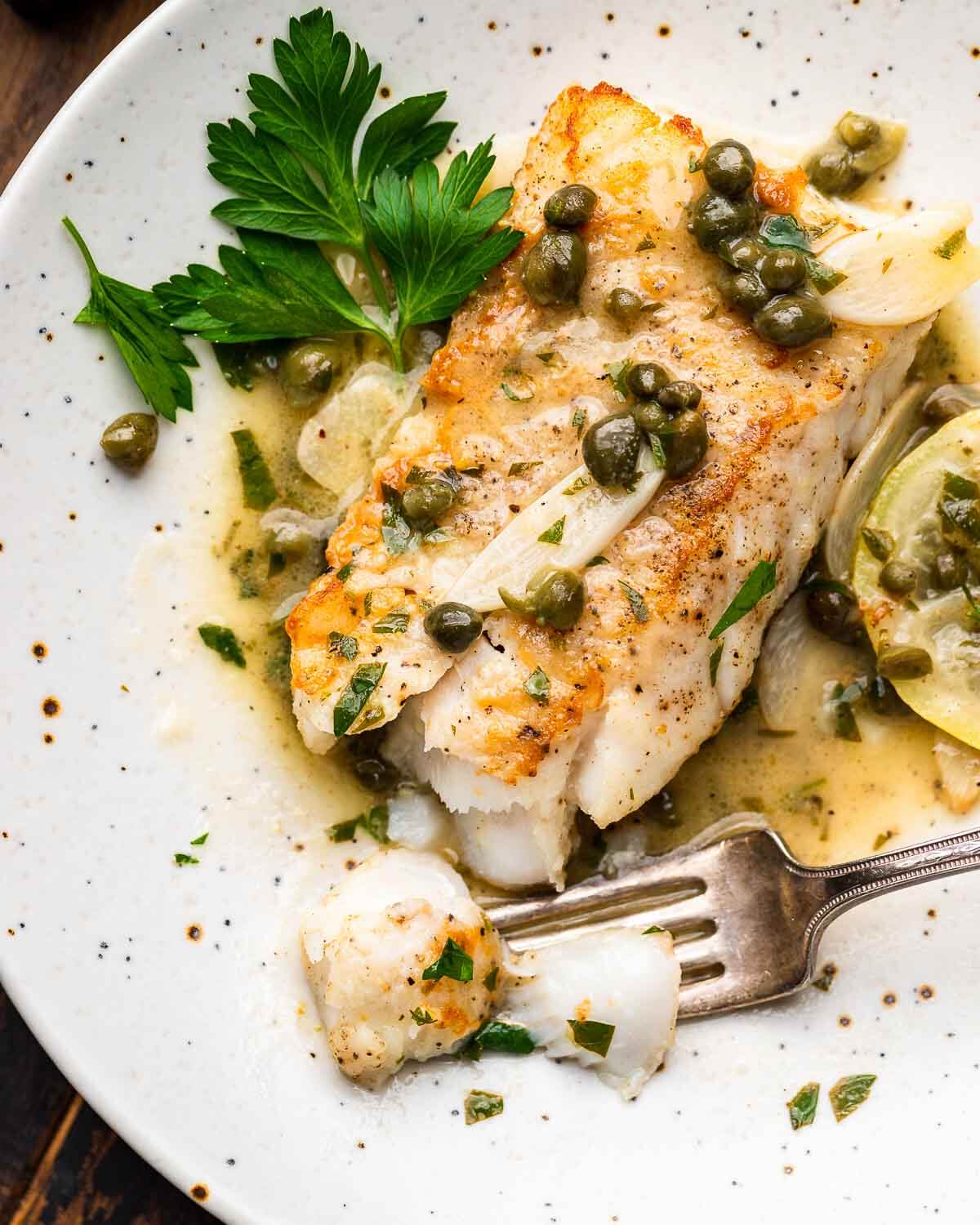 A cut piece of cod piccata in white plate.