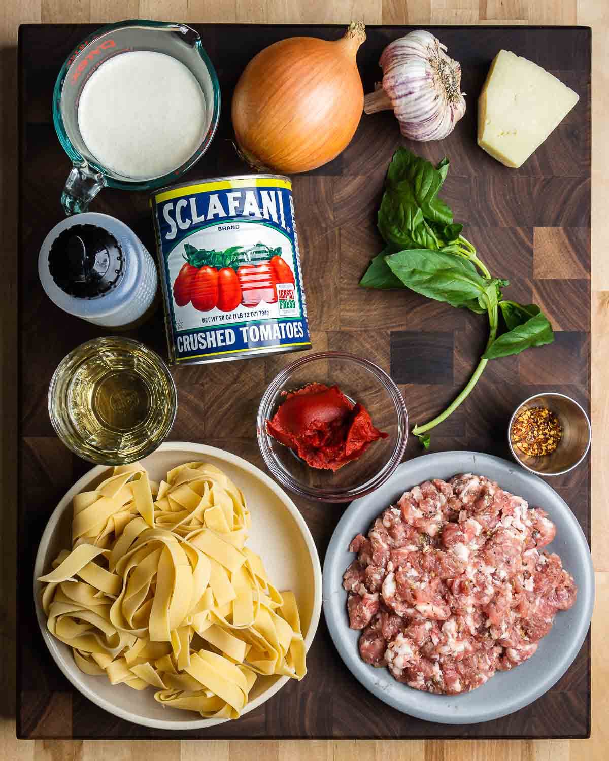 Ingredients shown: heavy cream, onion, garlic, Romano cheese, olive oil, canned tomatoes, white wine, tomato paste, basil, hot red pepper flakes, pappardelle pasta, and bulk fennel Italian sausage.
