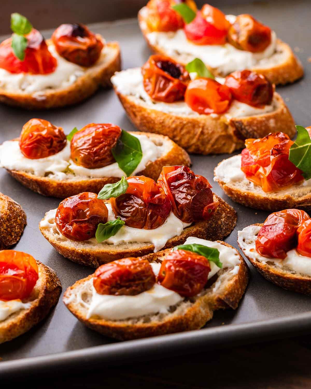 A bunch of ricotta roasted cherry tomato crostinis on a baking sheet.