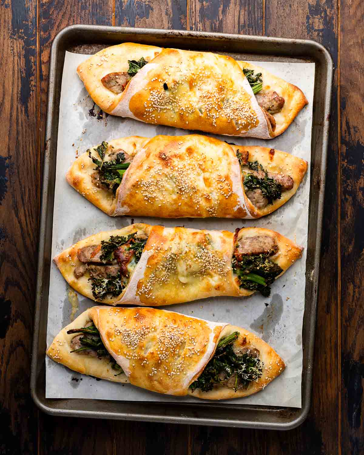 Overhead shot of four sausage broccoli rabe rolls on parchment paper lined baking sheet.