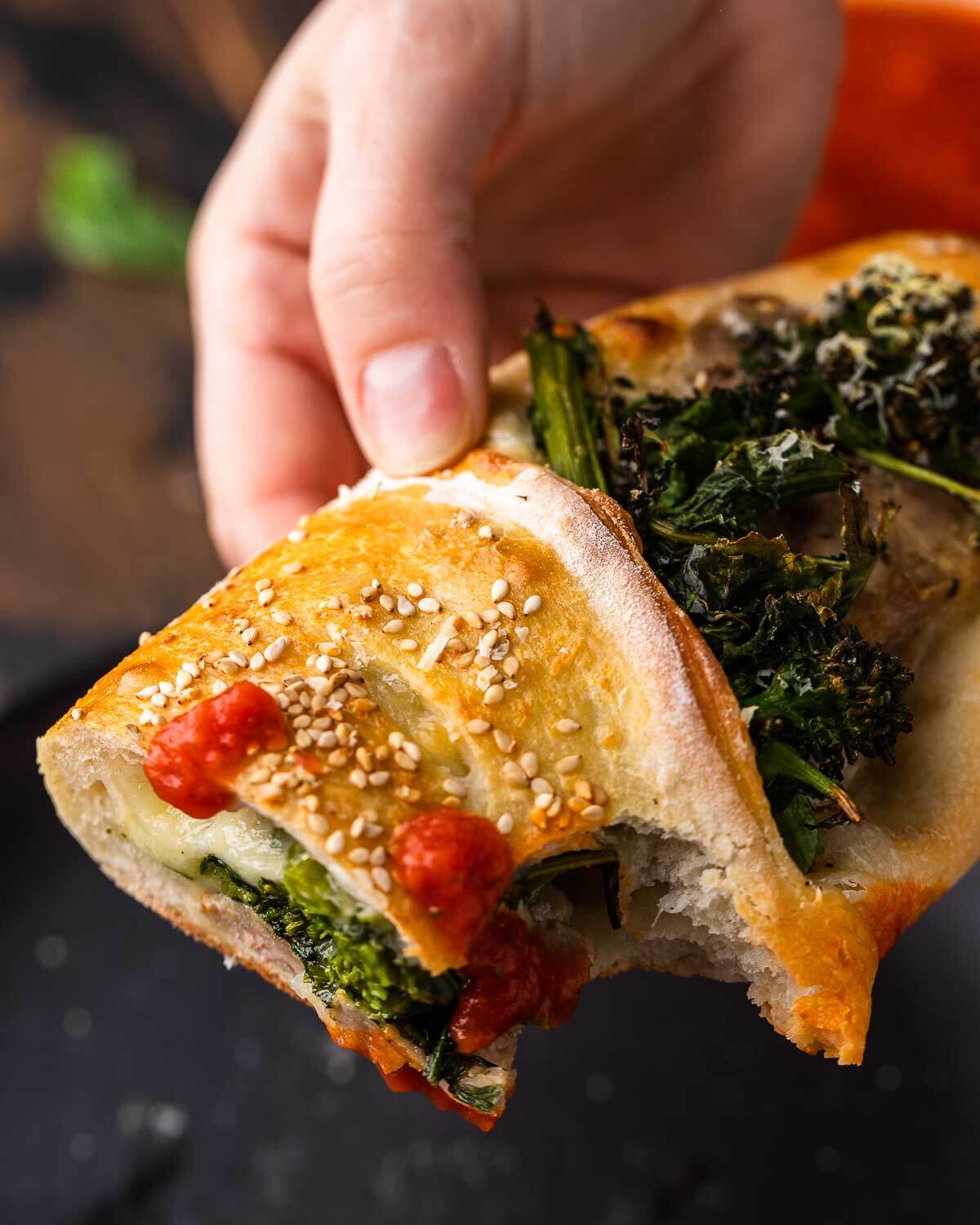 Hands holding sausage broccoli rabe roll dipped in sauce.