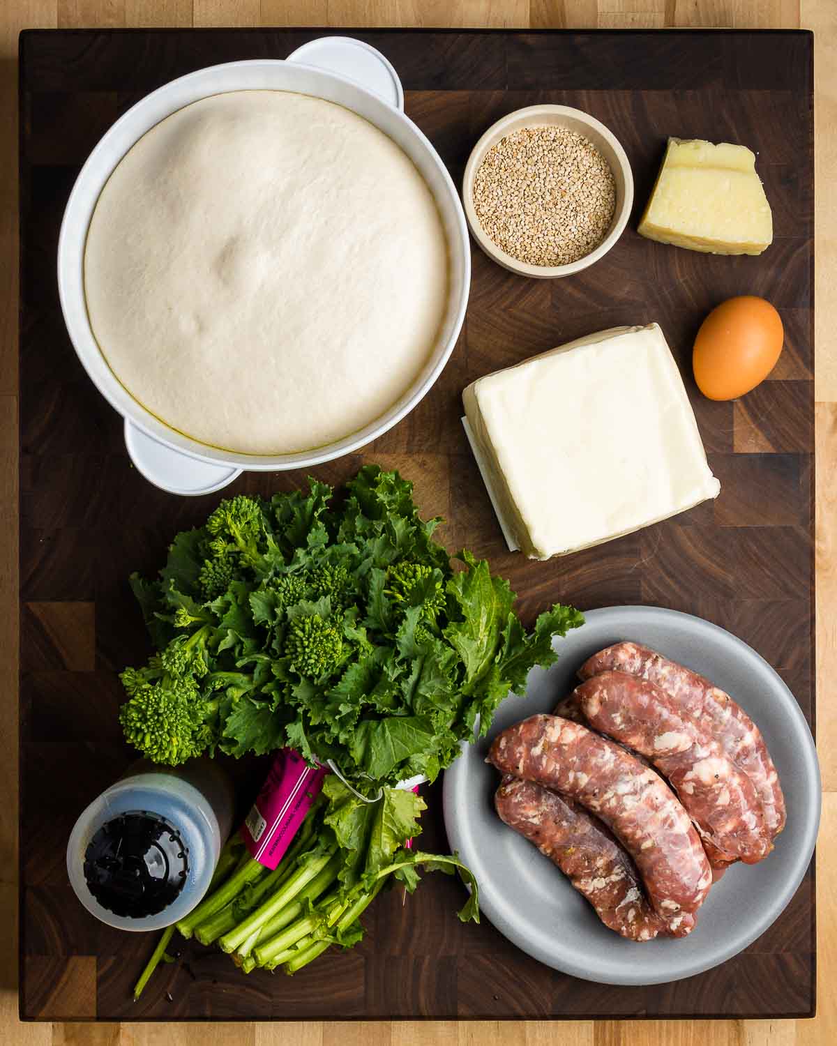 Ingredients shown: pizza dough, sesame seeds, Pecorino, mozzarella, egg, olive oil, broccoli rabe, and sausage links.