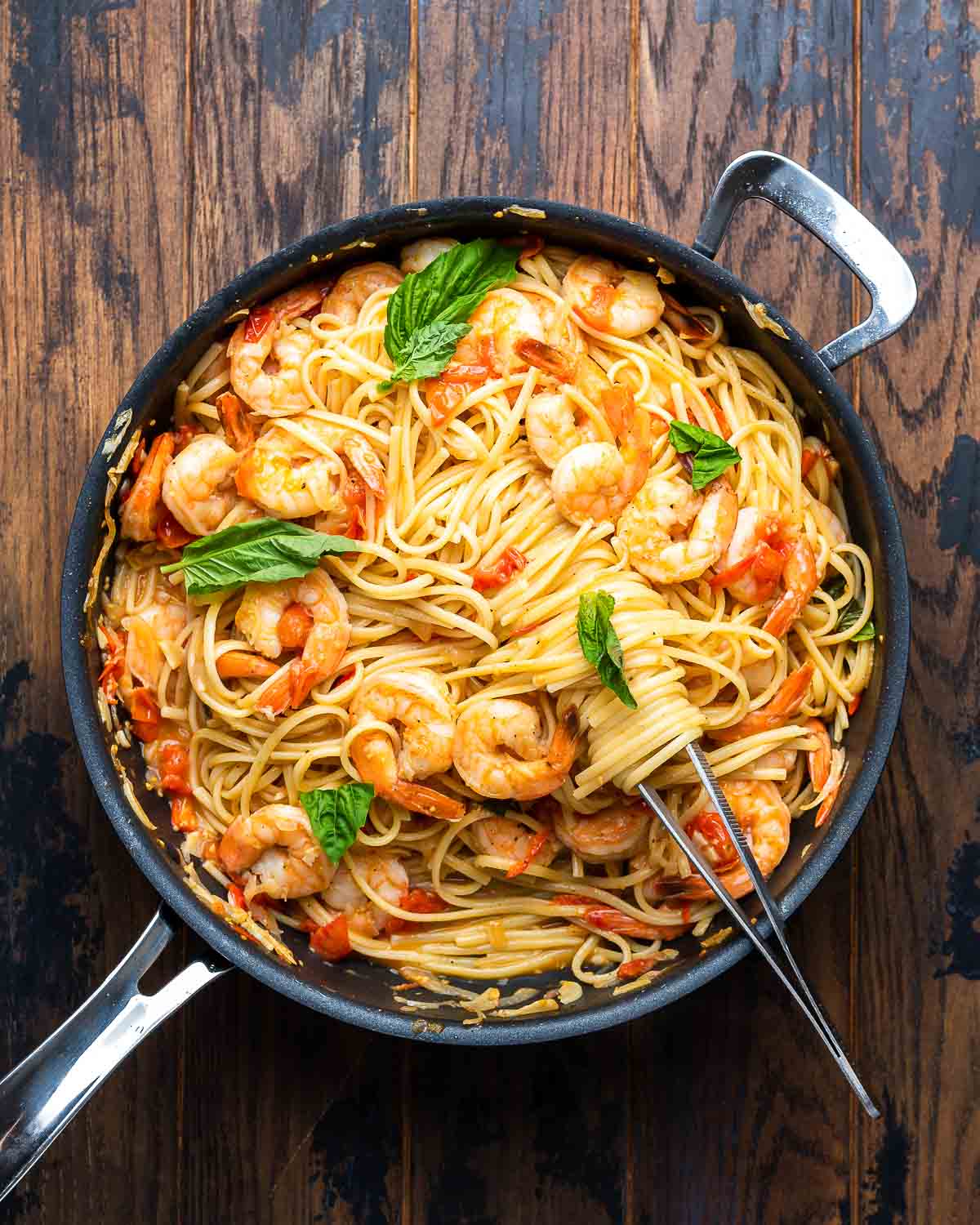 Overhead shot of shrimp tomato basil pasta in black pan on wood board.