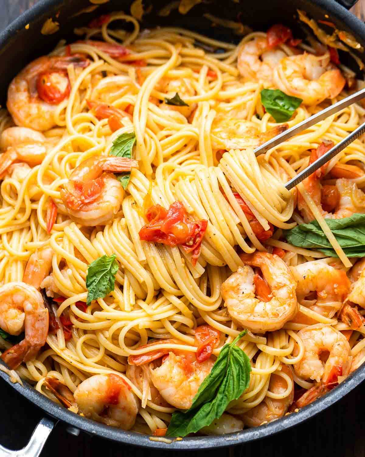 Shrimp tomato basil pasta in black pan with kitchen tweezers.