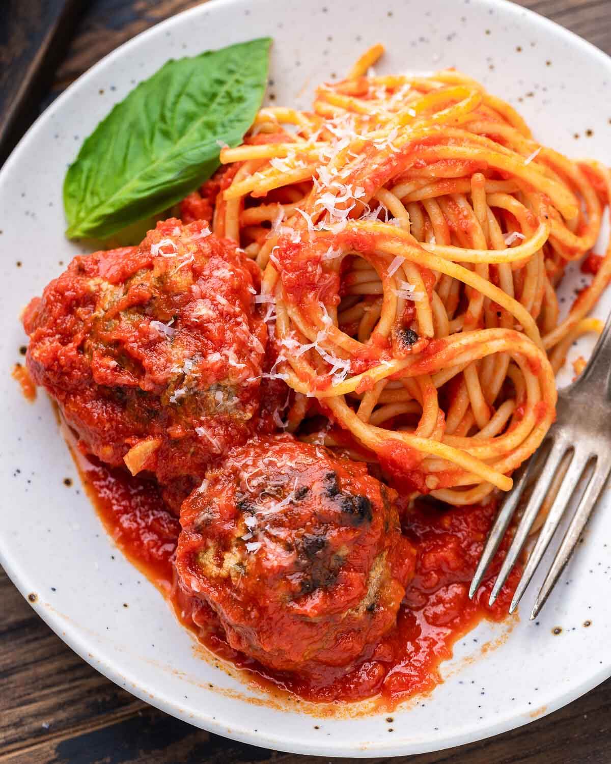 Spaghetti and meatballs on white plate with basil garnish.