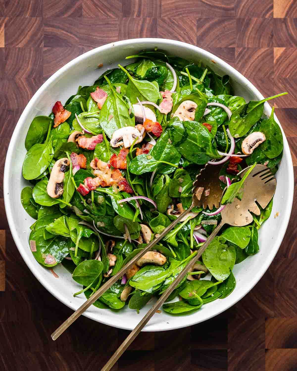 Overhead shot of large white bowl with spinach salad with hot bacon dressing.