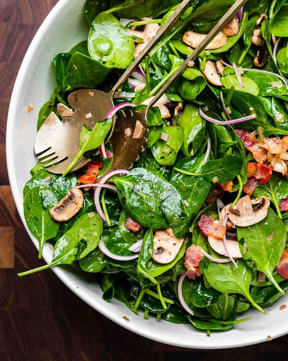 Closeup shot of large white bowl with spinach salad with hot bacon dressing.
