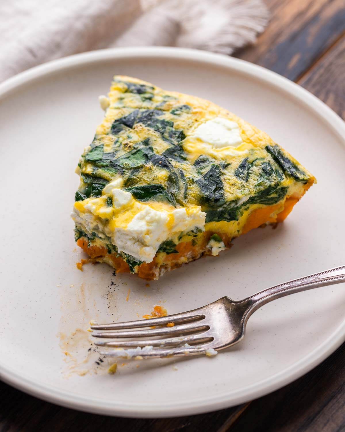 Sweet potato and goat cheese frittata in white plate with a bite taken out of it.