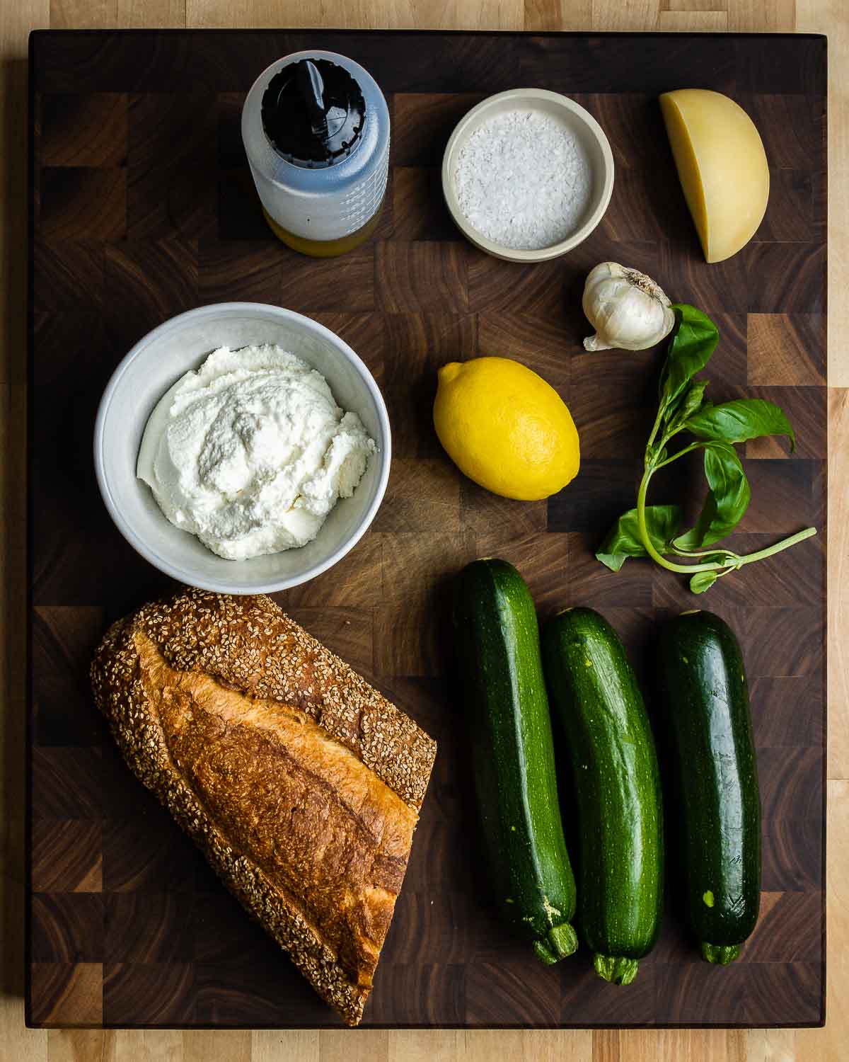Ingredients shown: extra virgin olive oil, flaky salt, garlic, caciocavallo cheese, ricotta, lemon, basil, bread, and zucchini.