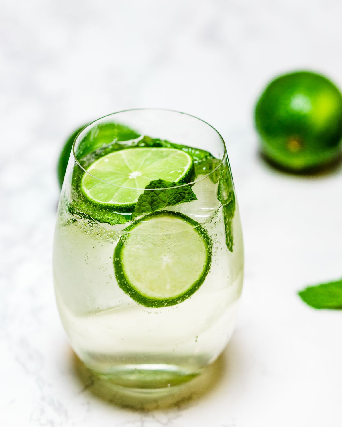 Hugo spritz cocktail with lime and mint garnish on white board.