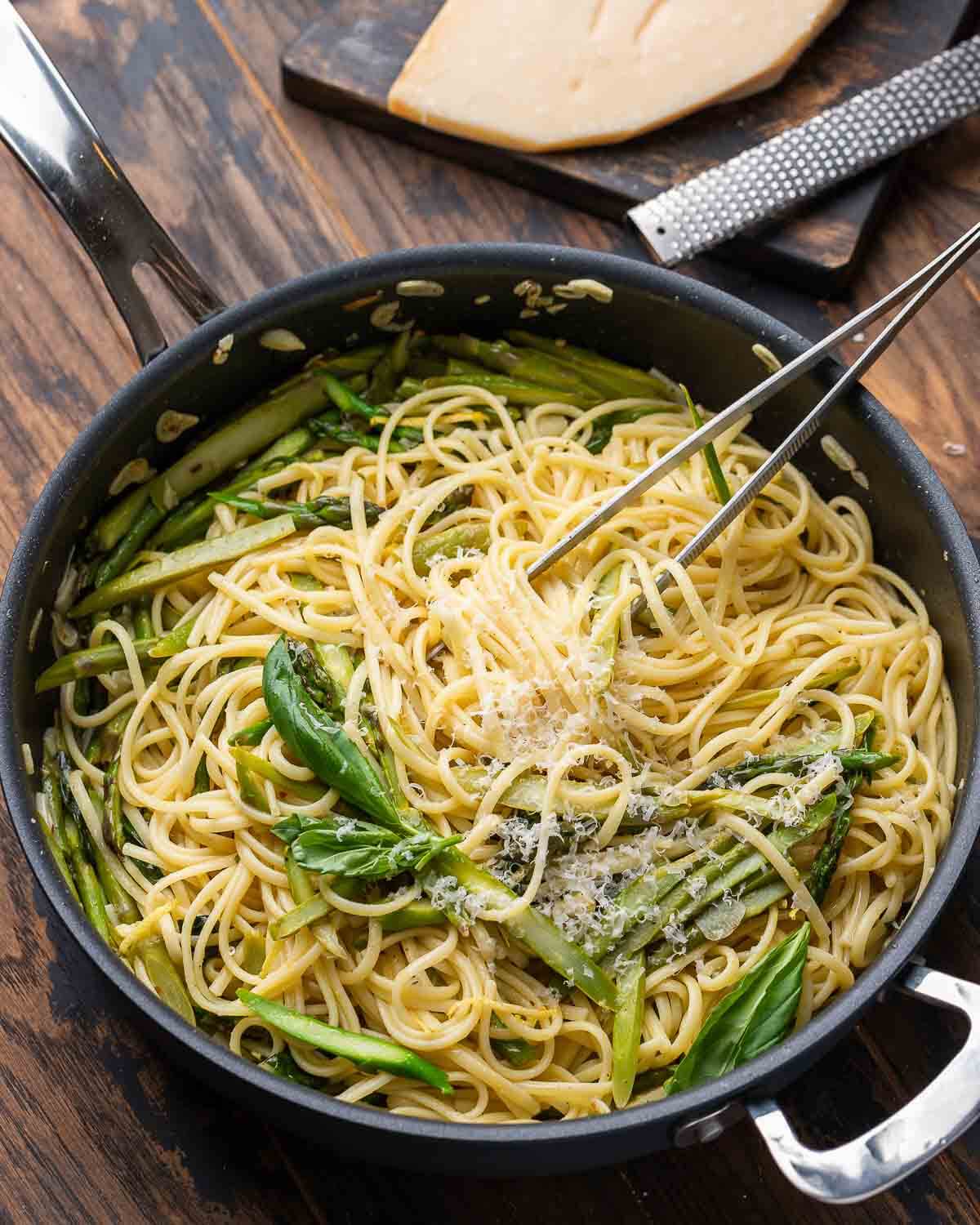 Black pan with lemon asparagus pasta along with block of parmesan cheese in the background.