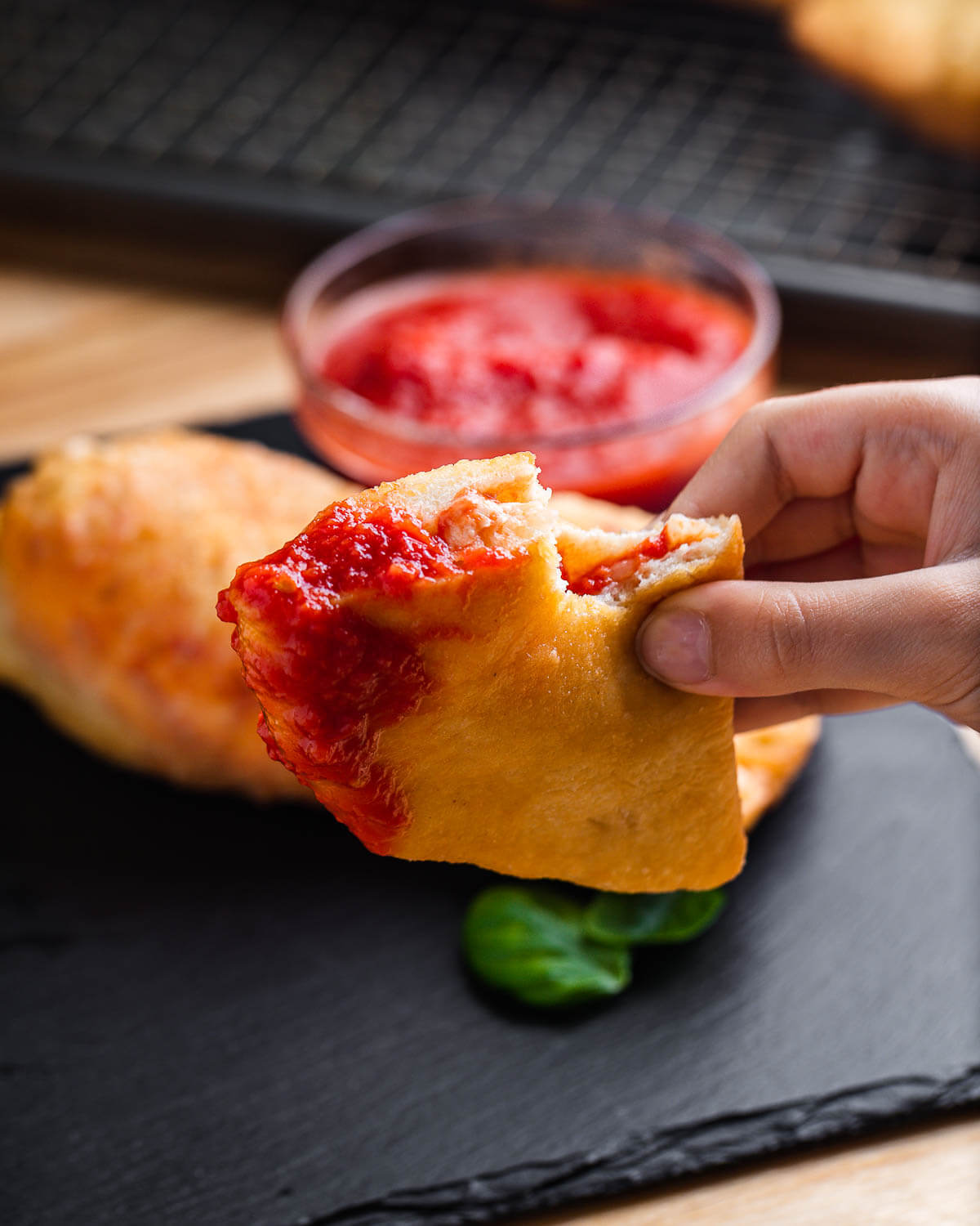 Hands holding a panzerotti dipped in marinara sauce.