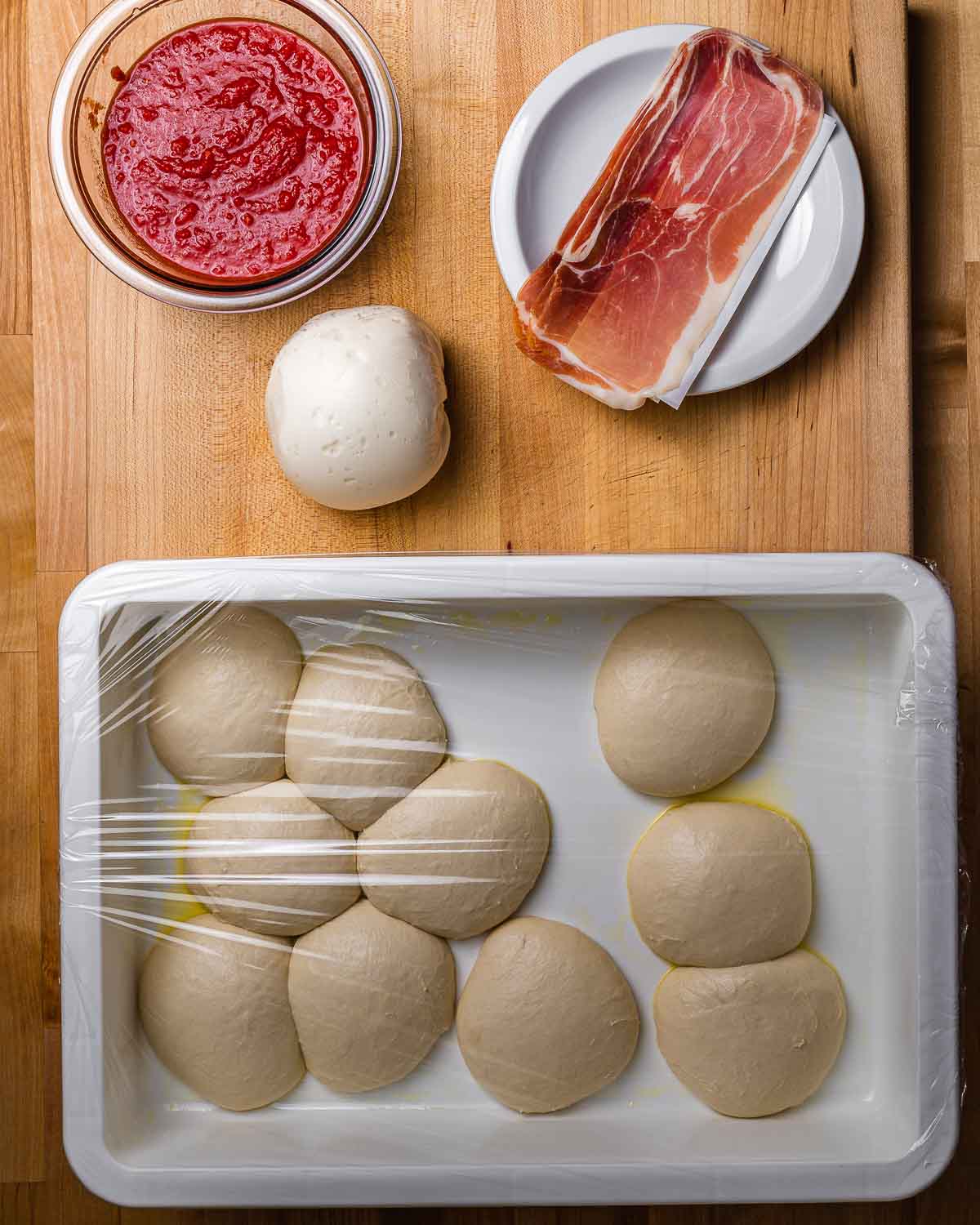 Ingredients shown: crushed tomatoes, fresh mozzarella ball, prosciutto, and 10 small dough balls.