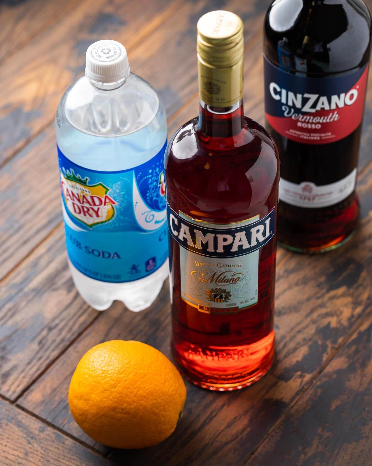Ingredients shown: club soda, sweet vermouth, campari, and an orange.